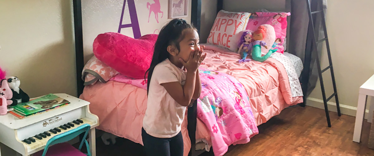 5-year-old Amy holds her hands over her mouth, surprised by the transformation of her bedroom.